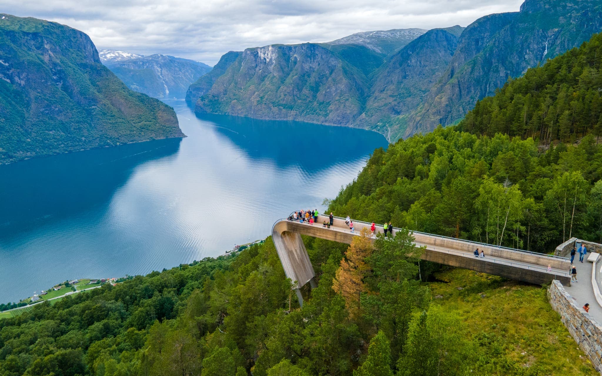 Narrow Naeroyfjord channel with steep mountain walls rising from calm water, small village at the fjord edge