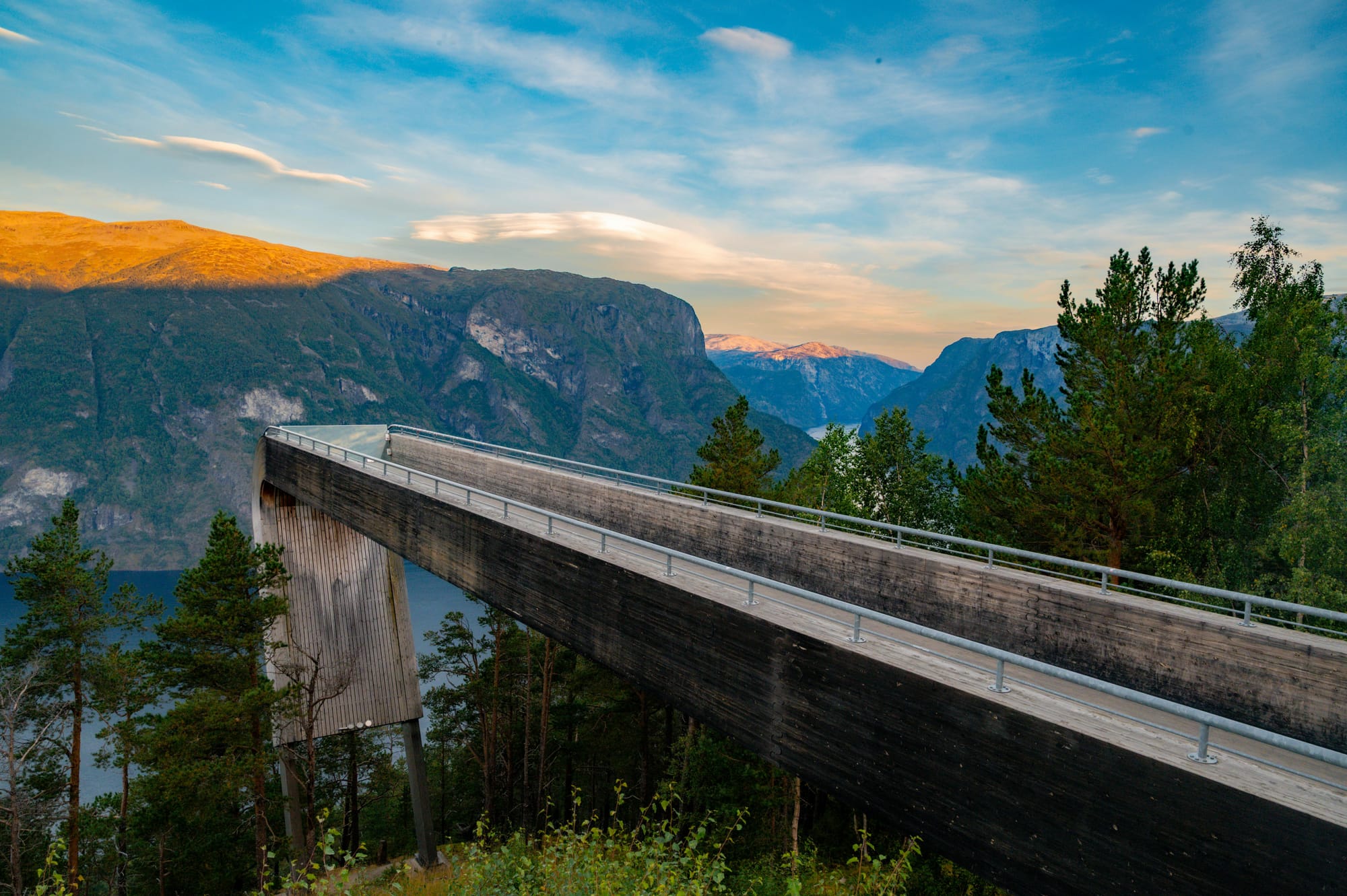 Stegastein viewing platform projecting out over Aurlandsfjord at 650 metres elevation, laminated wooden structure with glass wall angling down toward the fjord