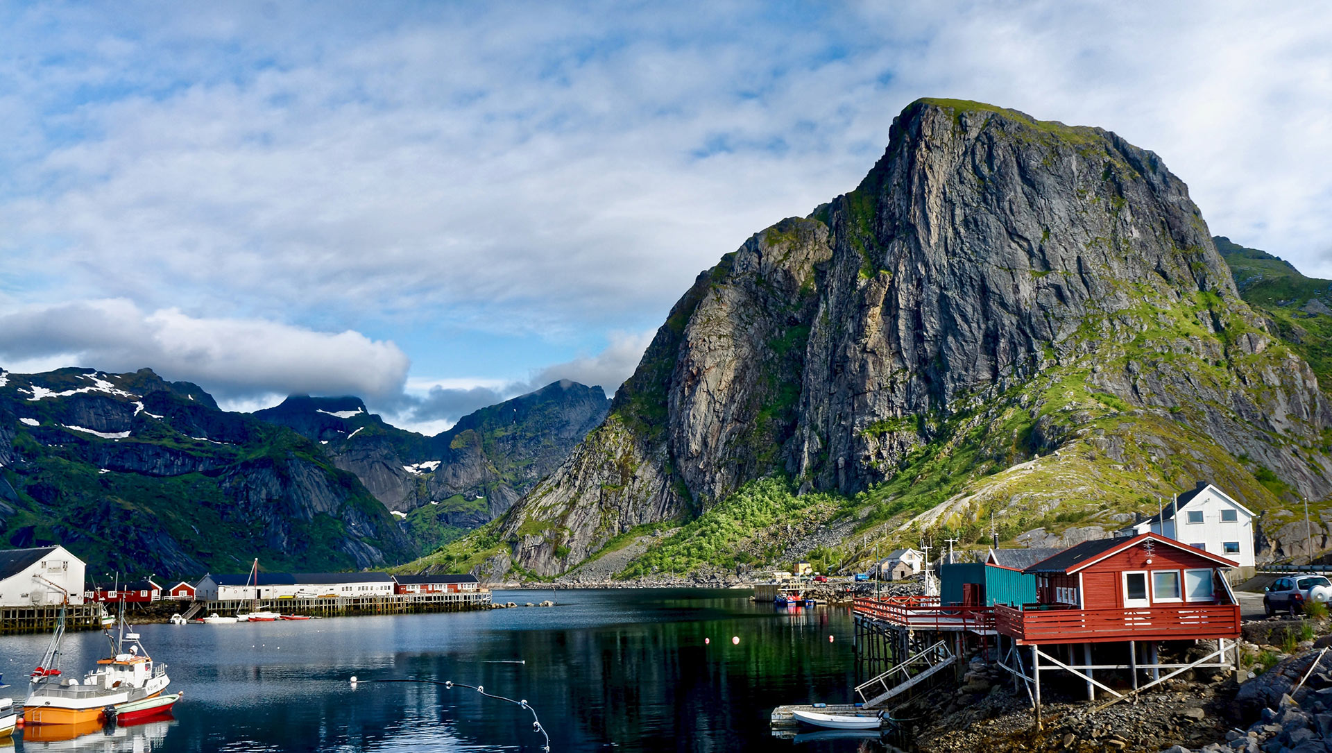 Red rorbu cabins on stilts and fishing boats in a Lofoten harbour below a sheer grey peak