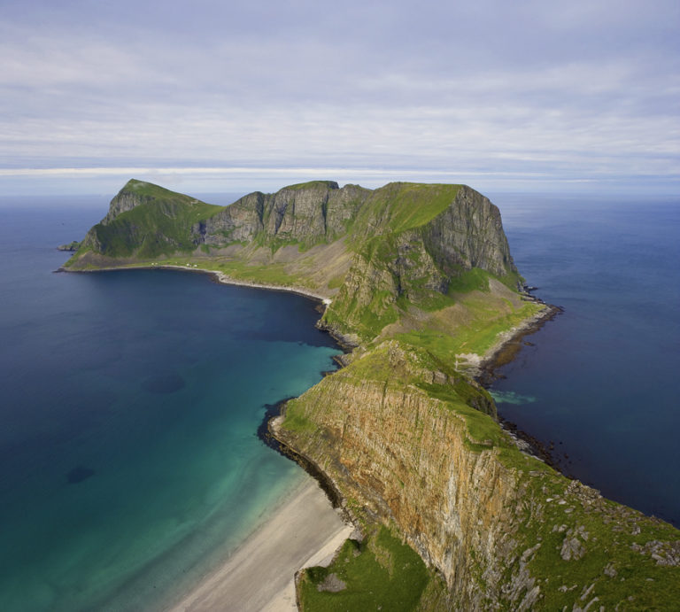 White sand beach surrounded by steep Lofoten peaks with blue Arctic water