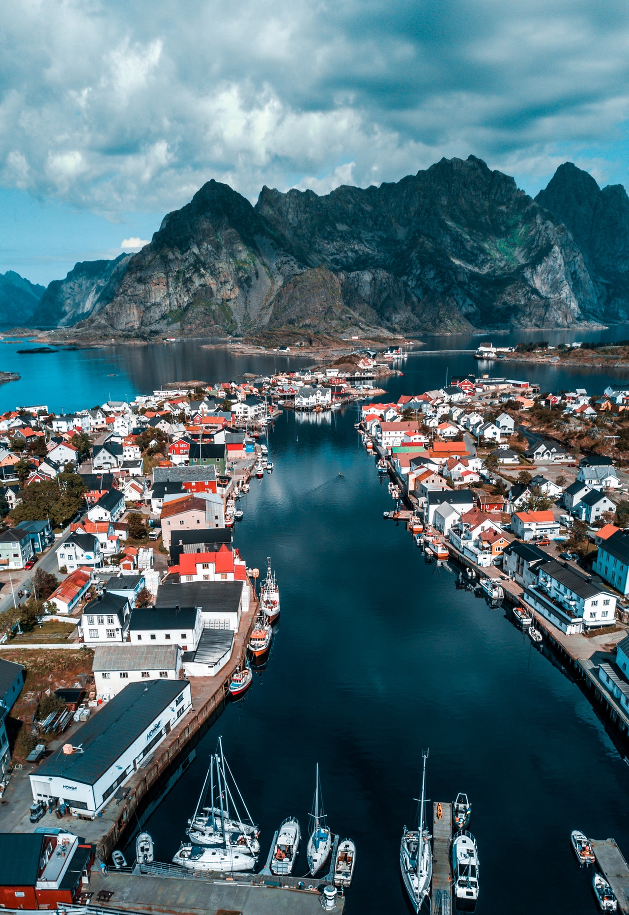 Aerial view of Henningsvær village spread across small islands connected by bridges, with the Festvågtind peak rising behind