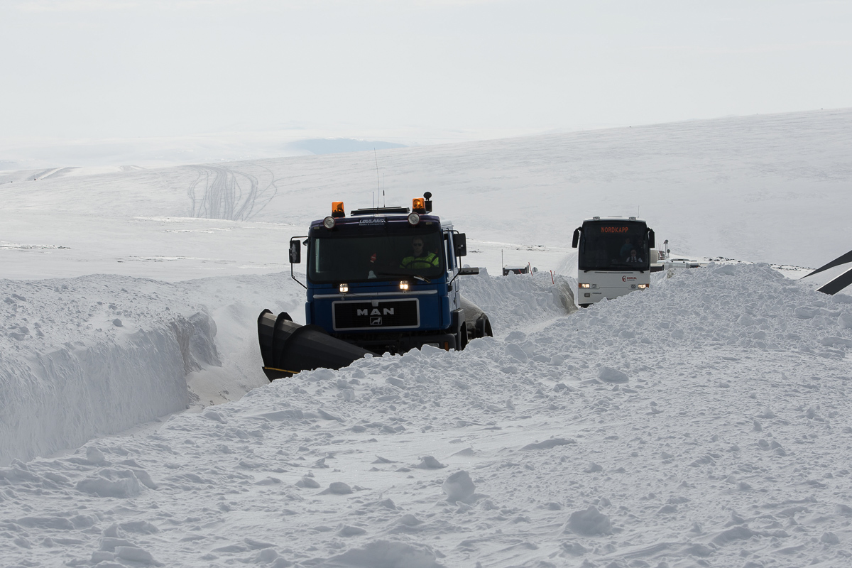 Snowplough leading a vehicle convoy through deep snow walls on the road to North Cape in winter