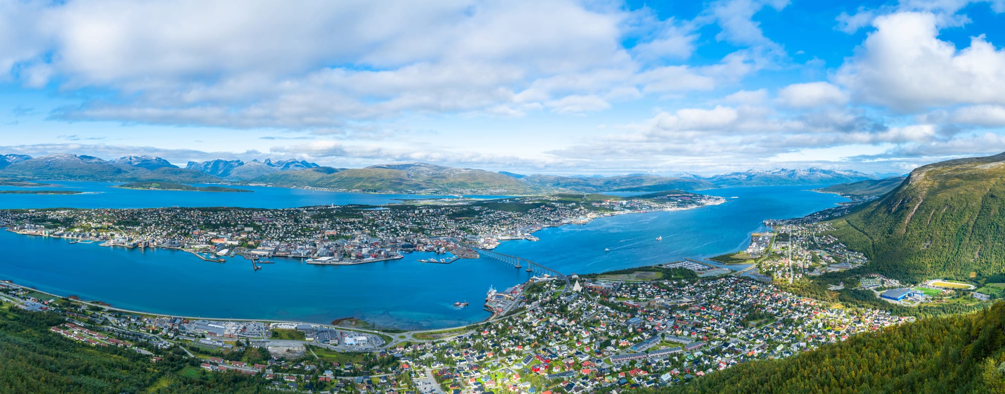 Tromsdalstinden peak rising above the Tromsdalen valley east of Tromsø, snow on the upper third of the mountain, blue sky and fjord visible